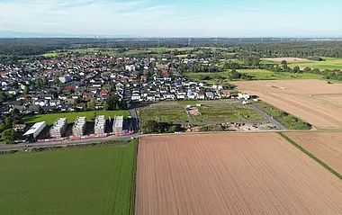 Luftaufnahme zeigt Felder und Wohngebiet mit Baustelle.