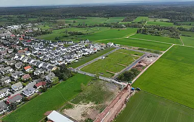 Luftaufnahme zeigt eine Baustelle mit angrenzenden Wohnhäusern und Feldern.