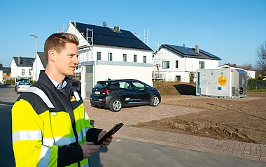 Techniker mit Tablet vor Einfamilienhäusern mit Photovoltaikanlage.
