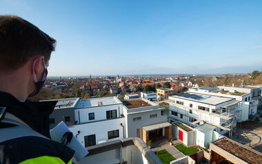 Blick über moderne Gebäude und eine Stadt im Hintergrund.