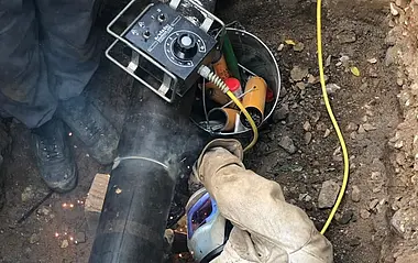 Ein e-netz-Monteur liegt seitlich neben einem Gasrohr in einer Grube.