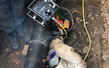 Ein e-netz-Monteur liegt seitlich neben einem Gasrohr in einer Grube.