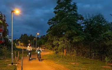 Zwei Radfahrer fahren nachts auf einem von LED-Leuchten erhellten Radweg