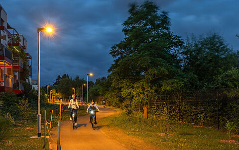 Zwei Radfahrer fahren nachts auf einem von LED-Leuchten erhellten Radweg