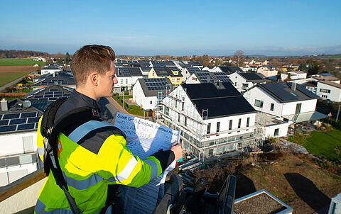 e-netz-Mitarbeiter hält einen Bebauungsplan in der Hand und blickt auf Neubauten der Solarsiedlung in Groß-Umstadt