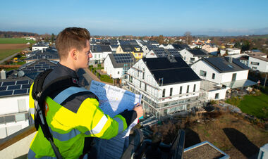 e-netz-Mitarbeiter hält einen Bebauungsplan in der Hand und blickt auf Neubauten der Solarsiedlung in Groß-Umstadt