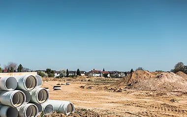 Rohransammlung auf einer Baustelle mit Wohngebiet im Hintergrund.