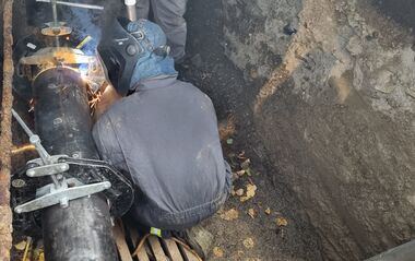 e-netz-Mitarbeiter sitzt in einer Grube und schweißt an einem Rohr.