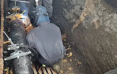 e-netz-Mitarbeiter sitzt in einer Grube und schweißt an einem Rohr.