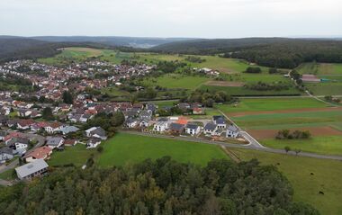 Luftaufnahme zeigt eine ländliche Siedlung mit Wohnhäusern und umliegenden Feldern.