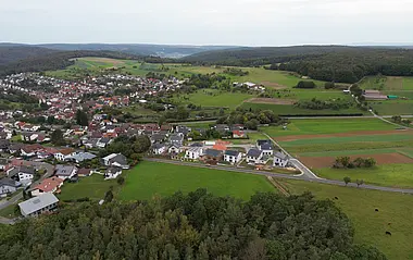 Luftaufnahme zeigt eine ländliche Siedlung mit Wohnhäusern und umliegenden Feldern.