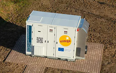 Energiespeicher „Entega Quartierspeicher Komplett“ mit EU-Förderlogo, steht auf einem gepflasterten Platz.