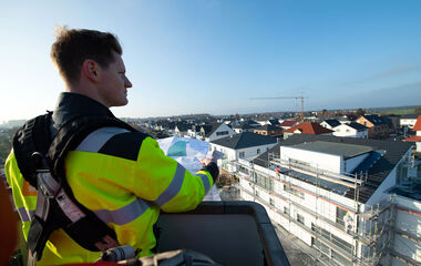e-netz Mitarbeiter mit Bauplan in der Hand auf einem Rohbau mit Blick auf die Stadt.