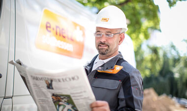 e-netz-Monteur steht vor einem Montagefahrzeug und liest die Tageszeitung Darmstädter Echo