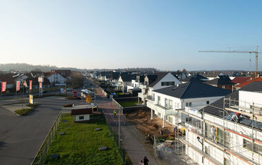 Neubaugebiet mit teils eingerüsteten Wohnhäusern, beleuchtet von hellem Sonnenlicht.