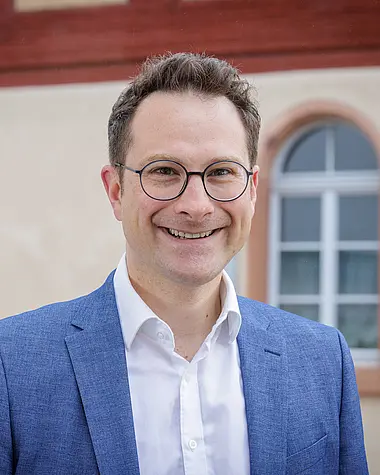 Bürgermeister Daniel Rauschenberger im Anzug und Hemd, lächelnd, mit Brille.