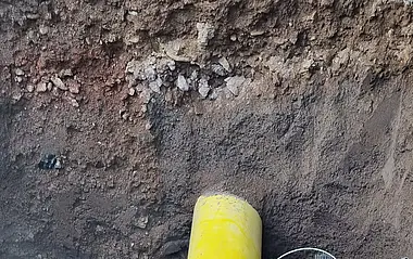 e-netz-Monteur liegt unter einem Gasrohr in einer Grube.