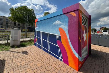 Bunt gestaltete Trafostation mit Blick auf eine Stadtlandschaft.