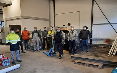 Eine Gruppe von Arbeitern mit Schutzmasken steht in einer Werkshalle.