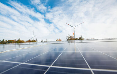 Solarmodule auf einem Dach mit Windkraftanlagen im Hintergrund.