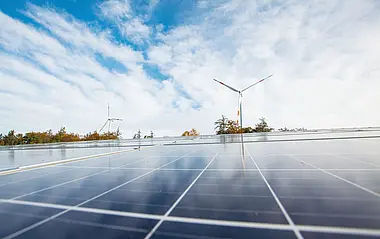 Solarmodule auf einem Dach mit Windkraftanlagen im Hintergrund.