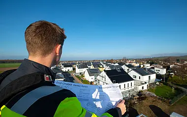 Ein e-netz-Mitarbeiter prüft Baupläne von einem Wohngebiet mit Solaranlagen.