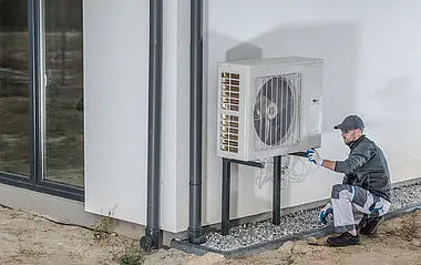 Ein Techniker installiert eine Wärmepumpe an einer weißen Fassade.