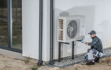 Ein Techniker installiert eine Wärmepumpe an einer weißen Fassade.