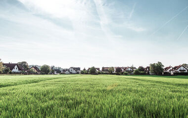 Wohngebiet mit Feldern im Vordergrund an einem sonnigen Tag.