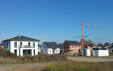 Neubaugebiet mit modernen Einfamilienhäusern und Photovoltaikanlagen, Baugerüst im Hintergrund.