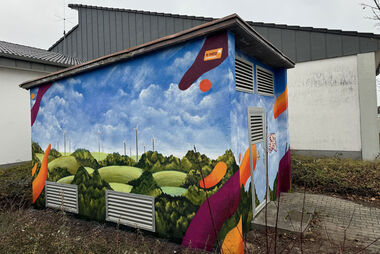 Gestaltete Trafostation mit Windkraftanlagen in einer hügeligen Landschaft bei bedecktem Himmel und e-netz Südhessen-Logo.