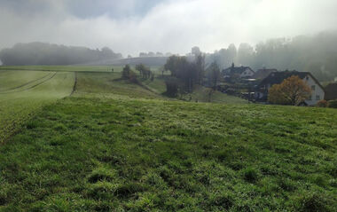 Grüne Hügellandschaft mit Dorf im Hintergrund, bedeckt von Nebel.