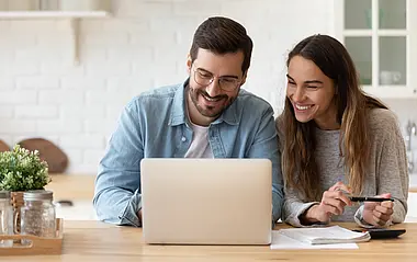 Mann und Frau sitzen vor einem Laptop in ihrer Küche