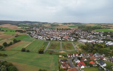 Luftaufnahme zeigt eine ländliche Szene mit Feldern, Wiesen und Häusern.