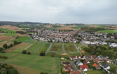 Luftaufnahme zeigt eine ländliche Szene mit Feldern, Wiesen und Häusern.