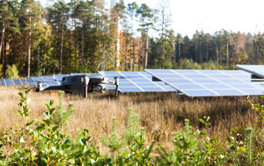 Eine Drohne schwebt über einem Solarpark inmitten einer grünen Landschaft. 