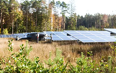 Eine Drohne schwebt über einem Solarpark inmitten einer grünen Landschaft. 