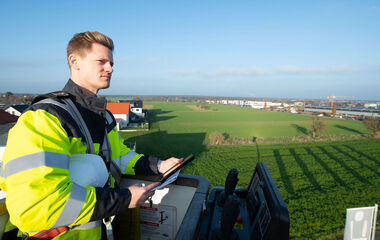 Ein Facharbeiter bedient ein Steuerungspult in der Höhe mit Blick auf eine Landschaft.