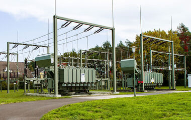 Umspannanlage mit Wohnhäusern und Bäumen im Hintergrund.