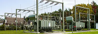 Umspannanlage mit Wohnhäusern und Bäumen im Hintergrund.