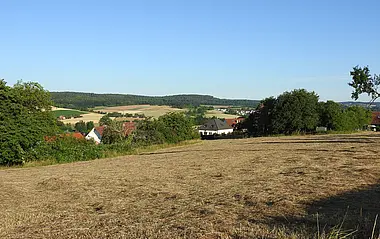 Erntewiese mit Blick auf ländliche Landschaft und entfernte Siedlungen.