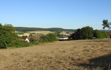 Erntewiese mit Blick auf ländliche Landschaft und entfernte Siedlungen.