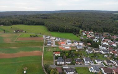 Luftaufnahme zeigt eine Wohnsiedlung mit Einfamilien- und Mehrfamilienhäusern und umliegender Grünfläche.