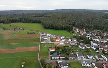 Luftaufnahme zeigt eine Wohnsiedlung mit Einfamilien- und Mehrfamilienhäusern und umliegender Grünfläche.